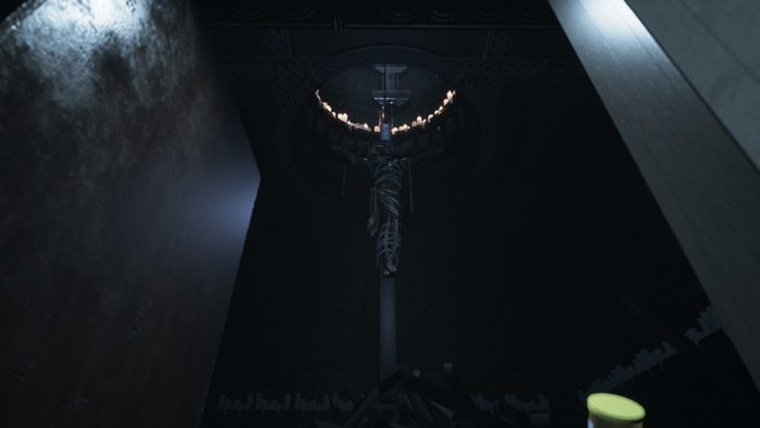 Une capture d'écran de Visage montrant un corps suspendu en forme de crucifixion sous un trou entouré de bougies.
