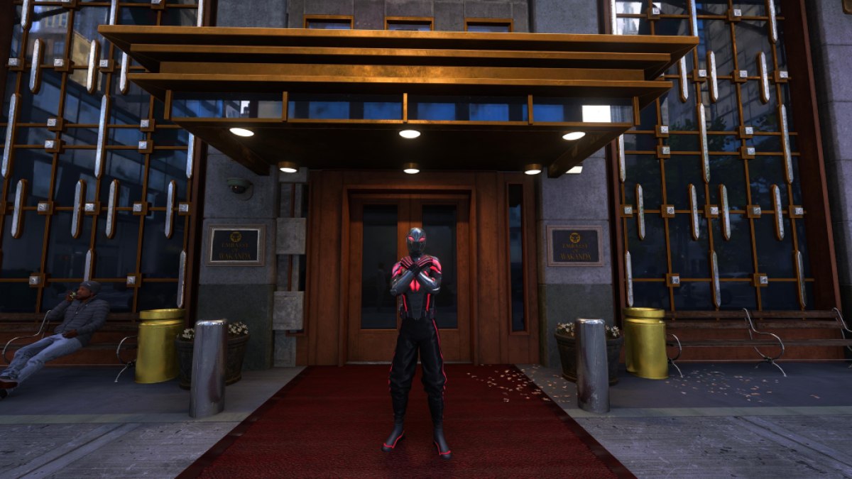Une image montrant Miles Morales devant l’ambassade du Wakandan faisant le salut wakandais.  Il porte son costume de style Wakanda.  L'image fait partie d'un article répertoriant tous les costumes de Miles Morales dans Marvel's Spider-Man 2 et comment les débloquer.
