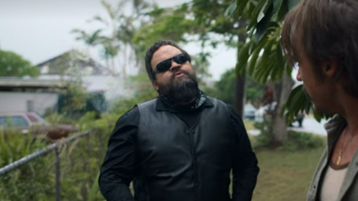 Un homme barbu et lunettes de soleil, dans une tenue de motard en cuir. 